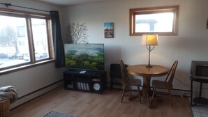 A living room with a TV, a dining table with chairs, a lamp, and a window with a view of the street. - Across from St Marys hospital Covered By Faith 1 (Rochester)