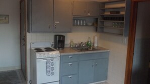 A compact kitchen with a white stove, grey cabinets, and a countertop with a coffee maker, dish soap, and a paper towel holder. - Across from St Marys hospital Covered By Faith 1 (Rochester)