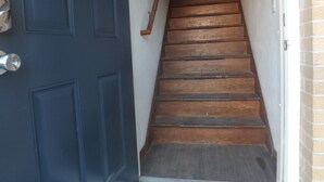 A wooden staircase with a dark blue door on the left and a brick wall on the right. - Across from St Marys hospital Covered By Faith 1 (Rochester)