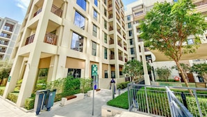 Un immeuble résidentiel à plusieurs étages, doté de balcons, d’une entrée sécurisée et d’un espace paysager avec des arbres.