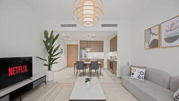Una sala de estar moderna con una televisión de pantalla plana, una mesa de centro, un sofá y un comedor con sillas.