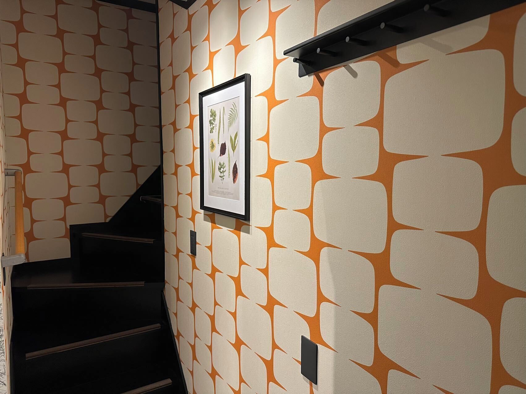 A staircase with a patterned wall and a framed botanical print.