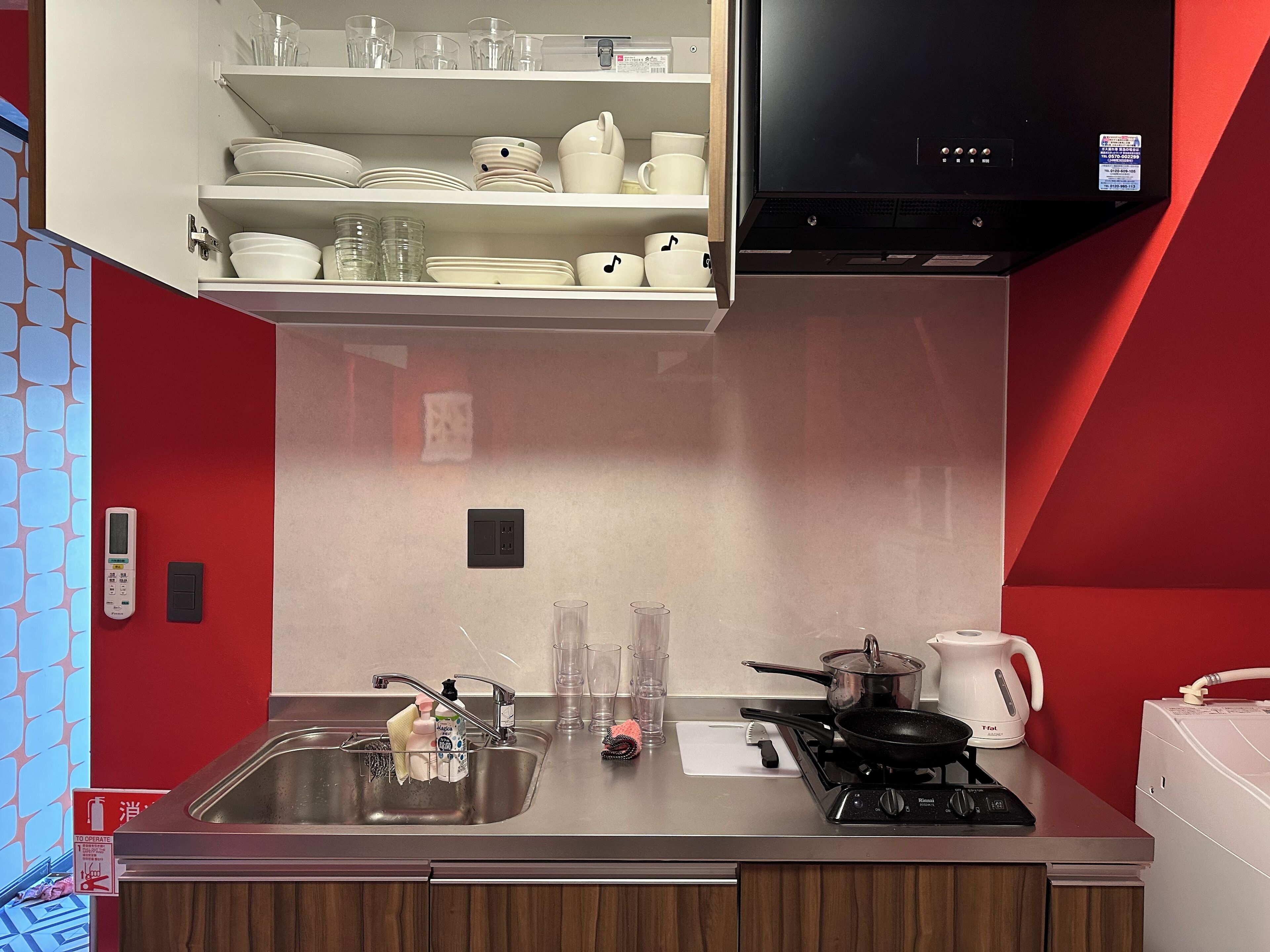A kitchen with a stainless steel sink, a stove, and a microwave. There are shelves above the sink holding dishes and glasses.