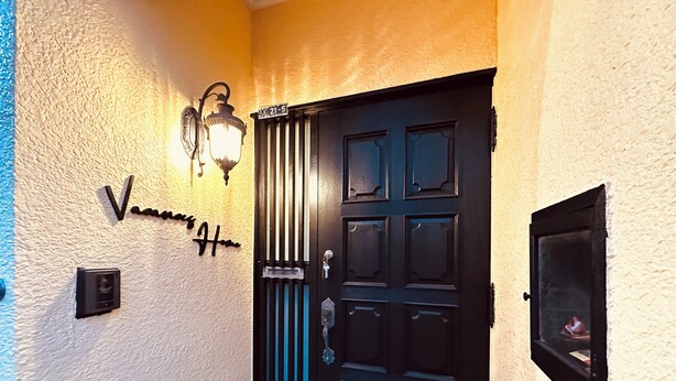Une porte noire avec un trou de serrure et une serrure, un luminaire fixé au mur et une petite boîte aux lettres.