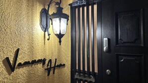 Une porte noire dotée d’un clavier pour l’ouverture, un luminaire fixé au mur et une enseigne au-dessus de la porte.