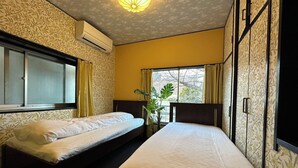 Une chambre avec deux lits simples, une fenêtre avec des rideaux, une plante en pot et un appareil de climatisation.