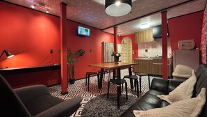 Un salon moderne avec un mur rouge, un canapé en cuir noir et une table à manger en bois.