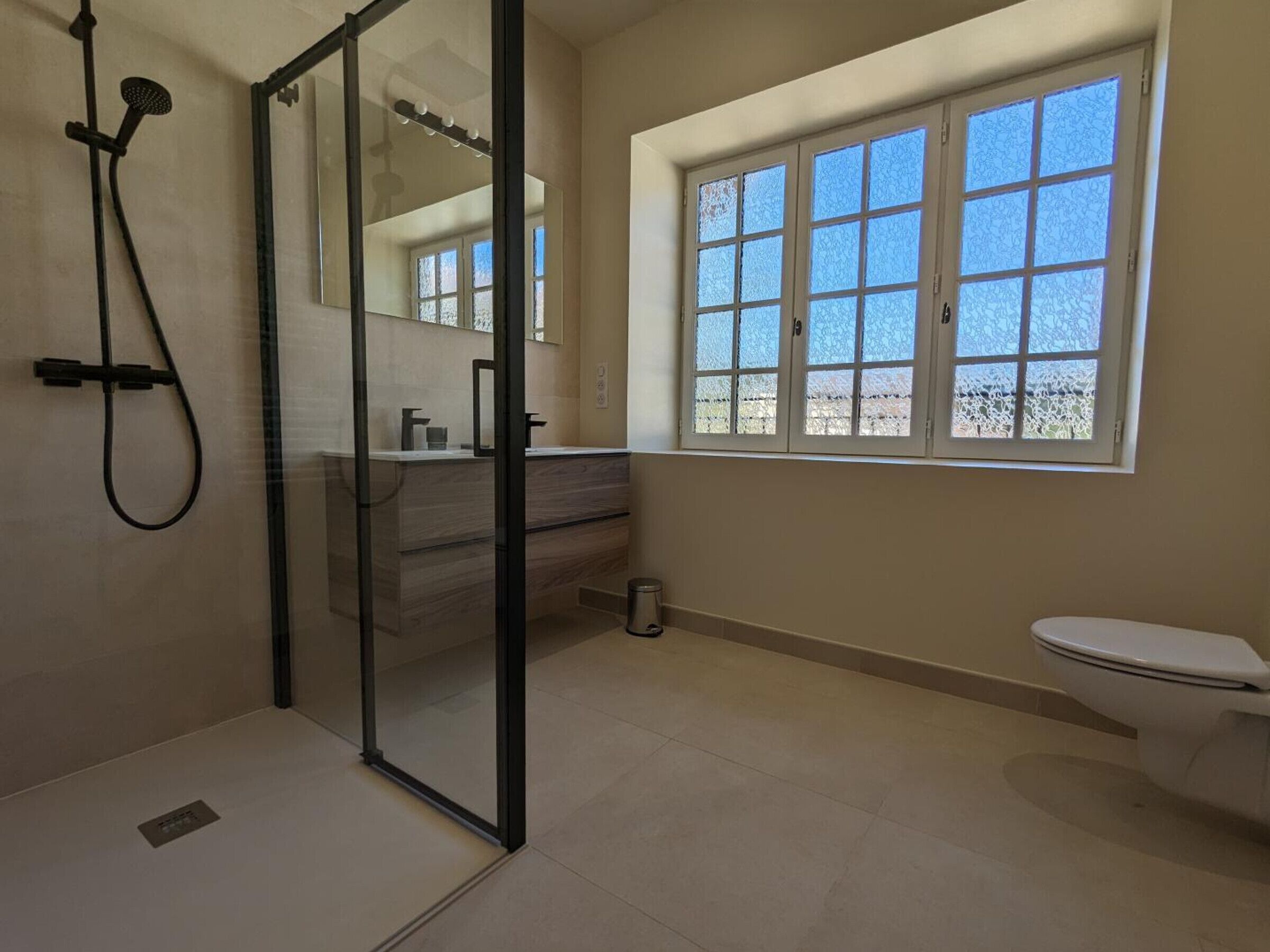 Une salle de bain avec une douche à parois de verre, des toilettes, un lavabo avec un miroir et une fenêtre en verre dépoli.