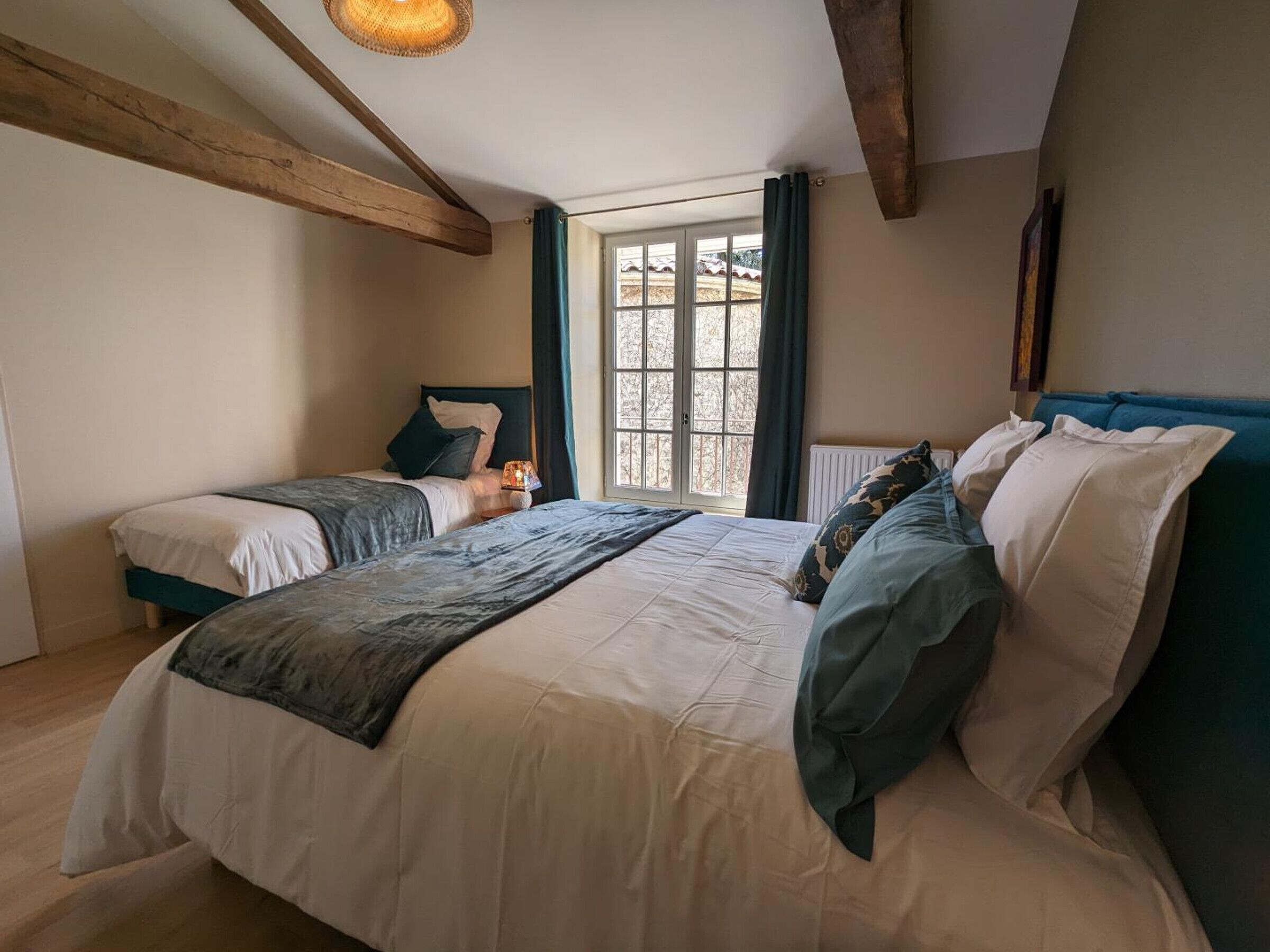 A bedroom with two beds, a large window, and wooden beams on the ceiling.