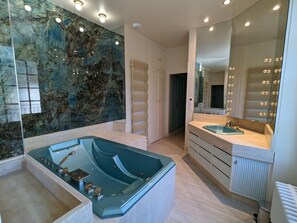 Une salle de bain moderne avec un mur en marbre, une baignoire sur pieds, un meuble-lavabo avec un miroir et une douche à l’italienne.
