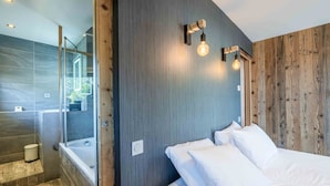 Une chambre moderne avec un grand lit, un mur d’accent en bois et une salle de bain dotée d’une douche à parois de verre.