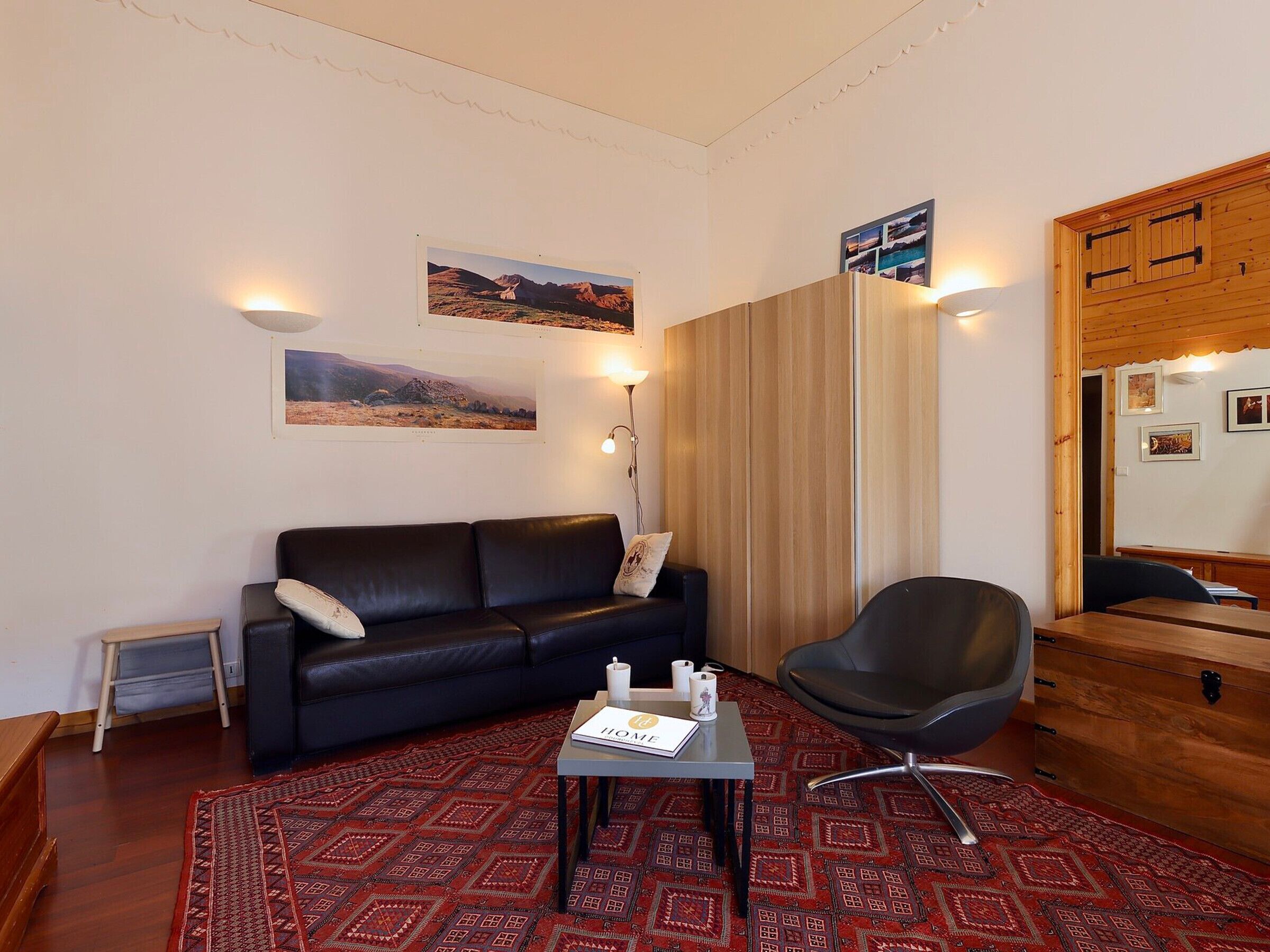 A room with a black leather sofa, a wooden cabinet, a black chair, and a patterned rug.