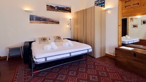 A bedroom with a bed, a wooden wardrobe, a mirror, and two wall-mounted lights. - Slope-side studio in Courchevel 1650 - Terrace with view (Courchevel)