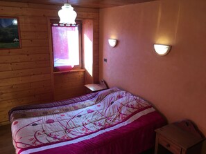 Une pièce en bois avec un lit, une fenêtre avec des rideaux et des lampes fixées au mur.