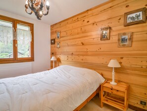 Quarto com parede de madeira, uma cama, duas mesas de cabeceira com luminárias e uma janela com cortinas.
