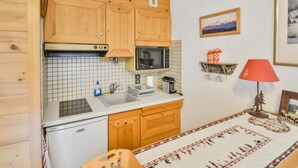 A compact kitchen with wooden cabinets, a microwave, a sink, and a small refrigerator.