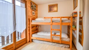 A bunk bed room with wooden walls, a window with curtains, and a bookshelf with books.