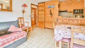 A cozy room with a sofa, a small table, and a kitchen area with wooden cabinets and a tiled backsplash.