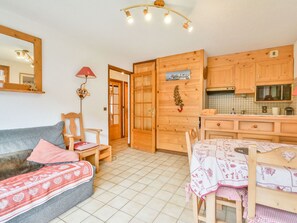 A cozy room with a sofa, a small table, and a kitchen area with wooden cabinets and a tiled backsplash. - Apartment in Morzine, 4 ppl, near cable cars (Morzine)