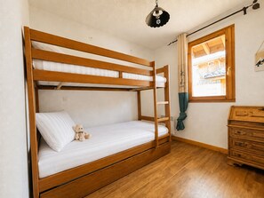 A bunk bed with a teddy bear, wooden dresser, and a window with curtains.