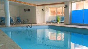 An indoor swimming pool with clear blue water, surrounded by lounge chairs and a tiled floor.