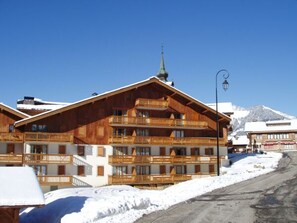 Un bâtiment en bois à plusieurs étages, doté de balcons, avec un clocher d’église et une montagne en arrière-plan.