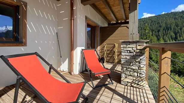 A wooden deck with two red lounge chairs, a stone wall, and a view of a forested mountain range. - Modern 2-room apartment + cabin, 4 persons, parking (Cohennoz)