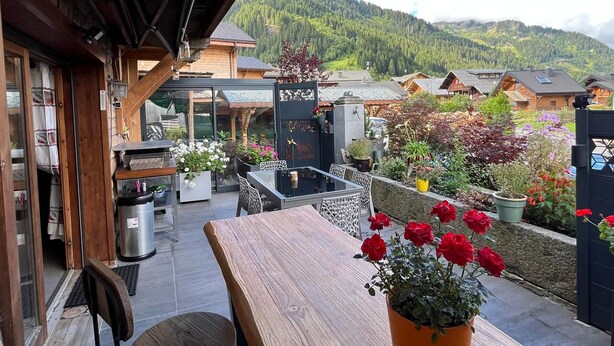 A wooden deck with a table and chairs, surrounded by potted plants and flowers. - Châtel: 3-Room Apt, Terrace, 5 Pers, Private Parking (Châtel)