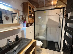 A modern bathroom with a glass-enclosed shower, a vanity with a black countertop, and a wooden cabinet above the mirror.