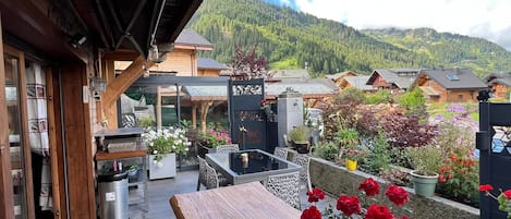 A wooden deck with a table and chairs, surrounded by potted plants and flowers.