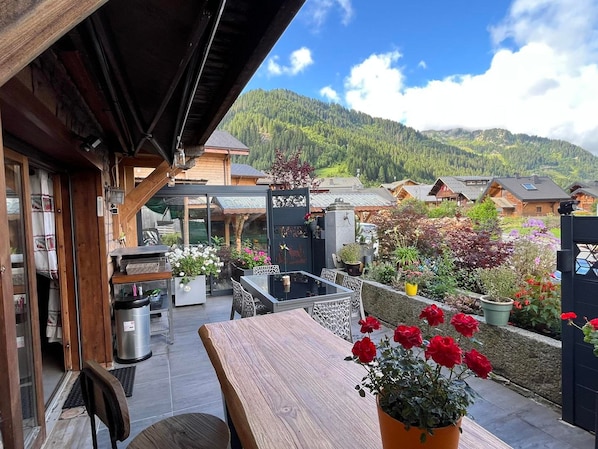A wooden deck with a table and chairs, surrounded by potted plants and flowers.