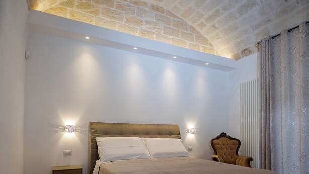 Ein Schlafzimmer mit einem großen Bett, einem Nachttisch, einem Sessel und einer Wandleuchte.