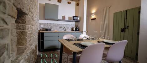 A cozy kitchen with a stone wall, wooden ceiling beams, and a dining area with a table set for two.