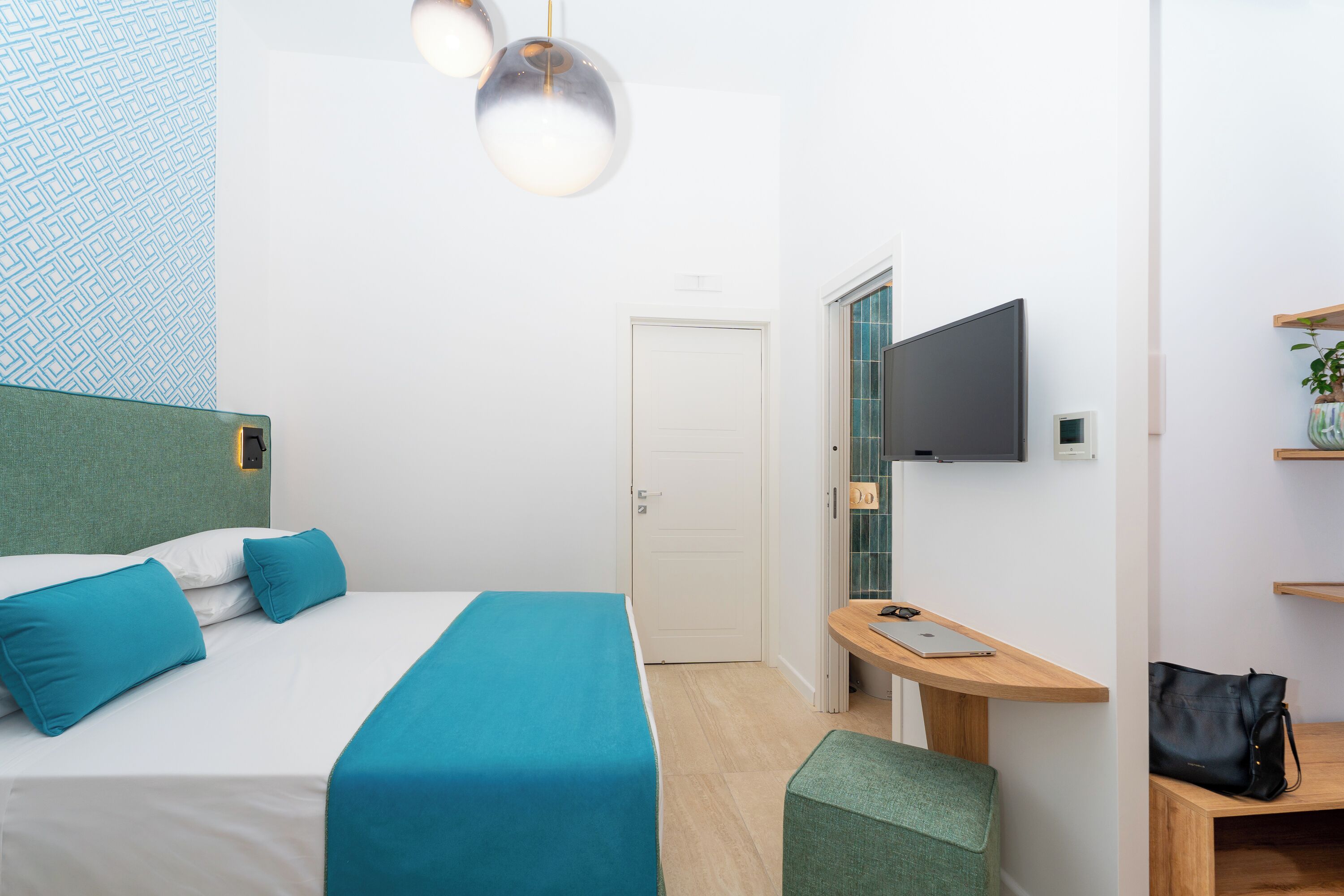 A modern hotel room with a bed, a desk, a TV, and a door.