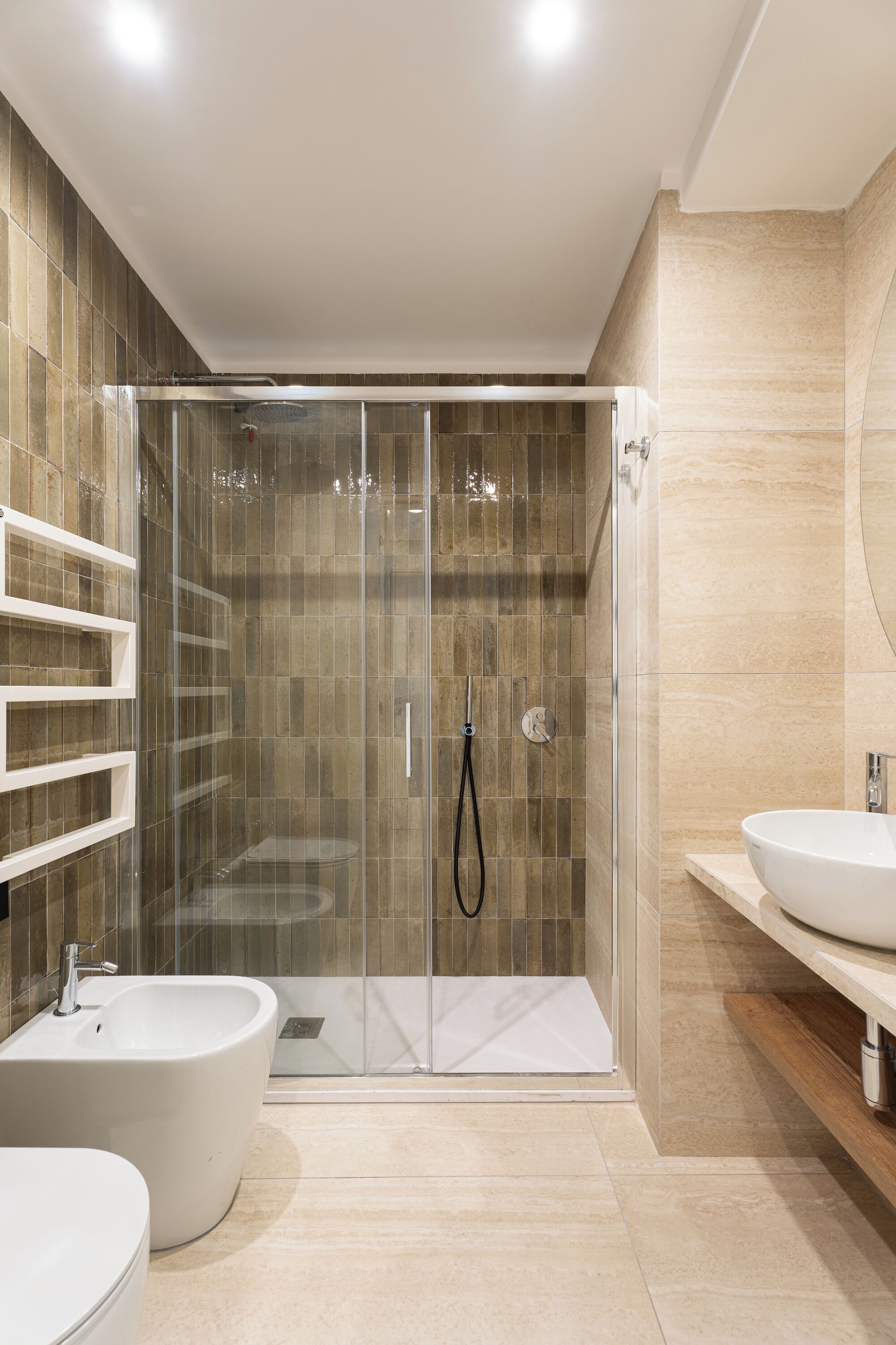 Un bagno moderno con cabina doccia in vetro, un bidet e due lavabi.