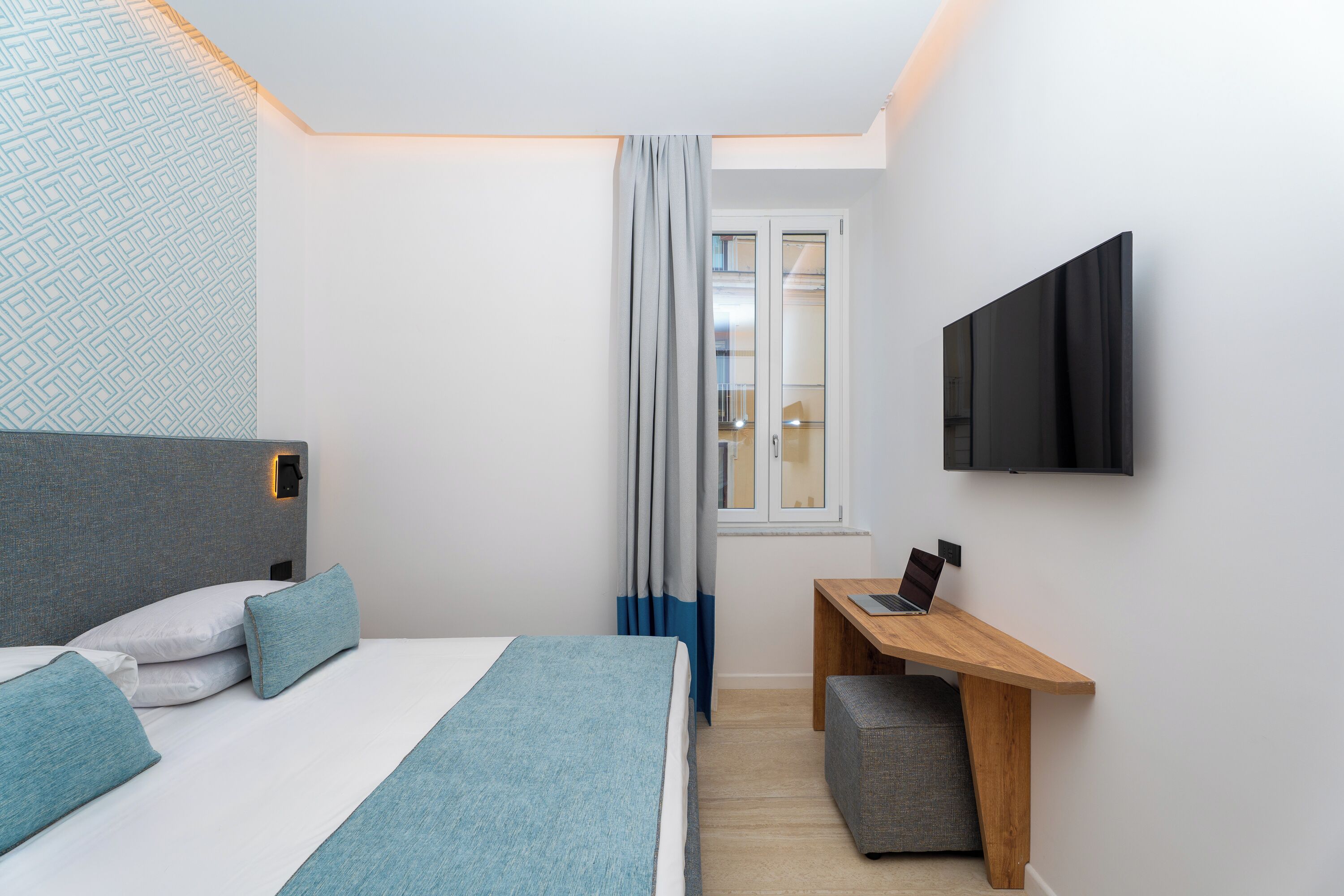 Une chambre d’hôtel moderne équipée d’un lit, d’un bureau, d’une télévision et d’une fenêtre avec des rideaux.
