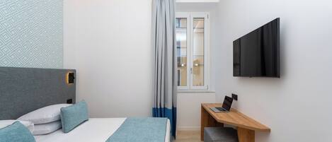 A modern hotel room with a bed, a desk, a TV, and a window with curtains.
