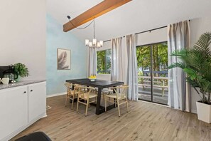 A modern kitchen with a dining area, wooden flooring, and a view of the outdoors.