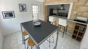 A modern kitchen with a stone wall, a dining area with a black table and wooden chairs, and a white pendant light. - The Loft Factory 4 Bedrooms Garonne View + Garden (Lormont)