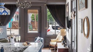 Una habitación amplia con una isla de mármol, un candelabro, un ventanal con cortinas, una silla, un televisor y un radiador.