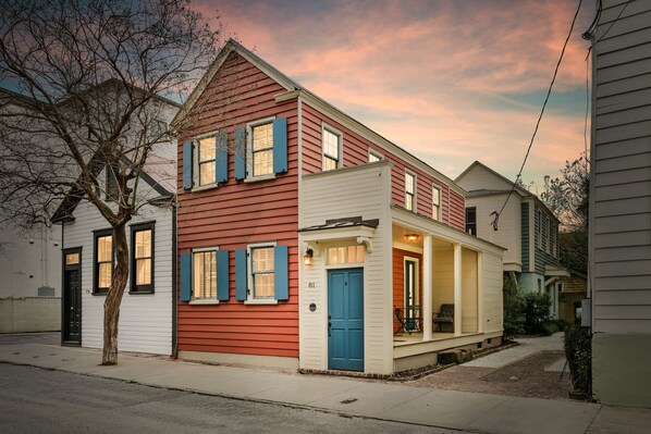 A two-story house with a red and white facade, a blue door, and a porch with outdoor seating.