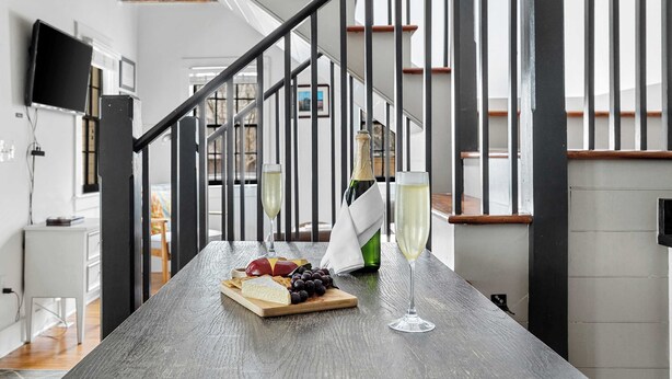 Een houten tafel met een kaasplank, druiven en een fles champagne in een modern interieur met een trap.