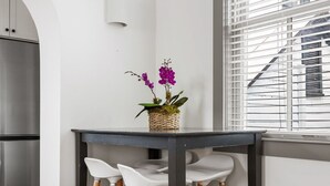 Una cocina con suelo de madera, una mesa negra con sillas blancas y un ventanal con persianas.
