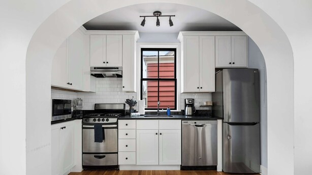 Una cocina moderna con armarios blancos, electrodomésticos de acero inoxidable y piso de madera.