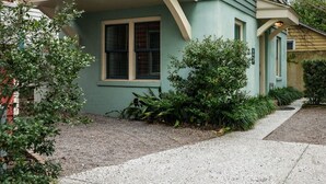 Un edificio residencial de dos plantas con entrada en esquina, un pequeño porche y un ventanal visible.