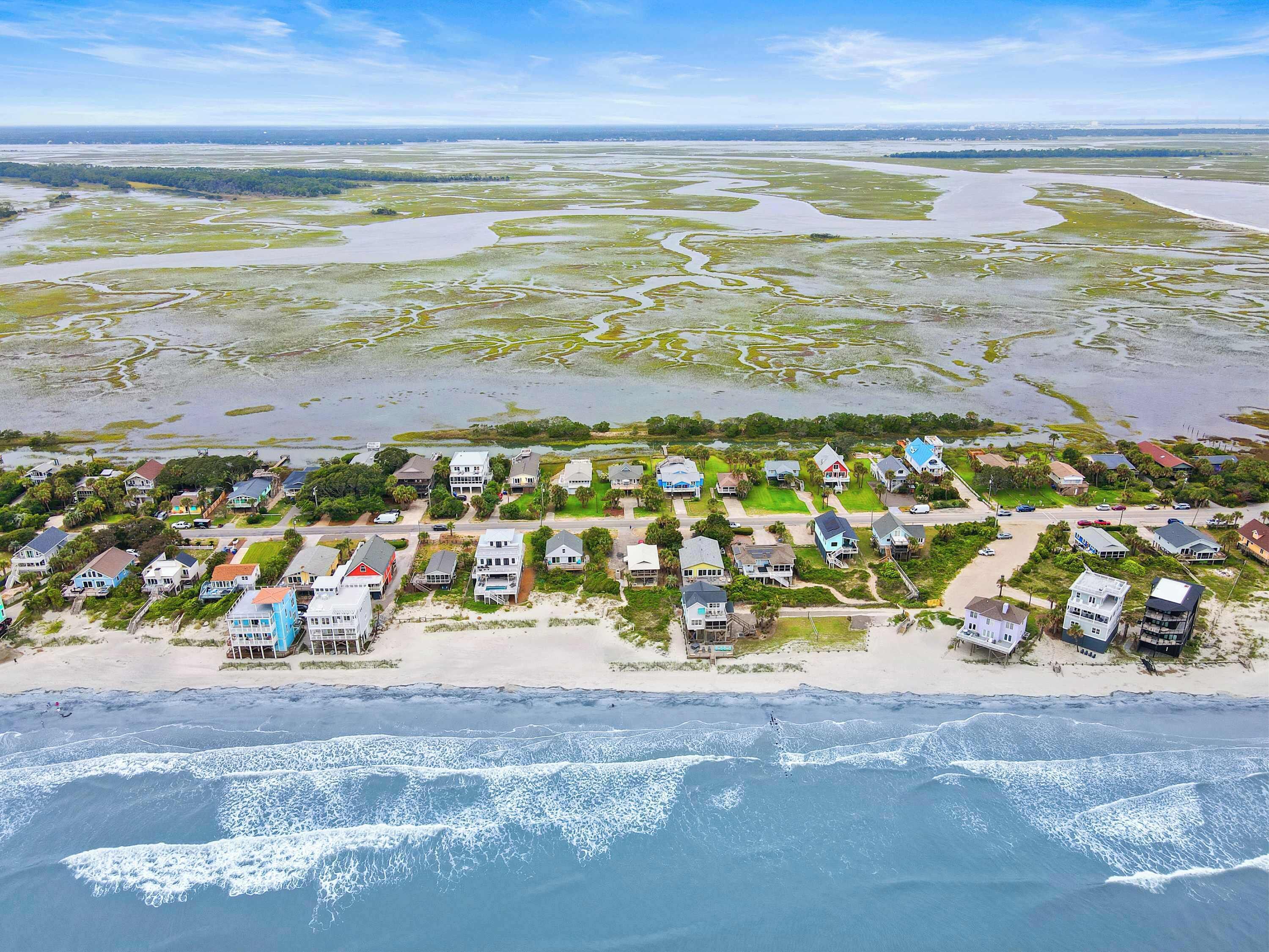 An aerial view of a coastal residential area with houses, a beach, and a marshy landscape.
