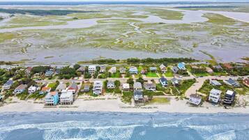 An aerial view of a coastal residential area with houses, a beach, and a marshy landscape.