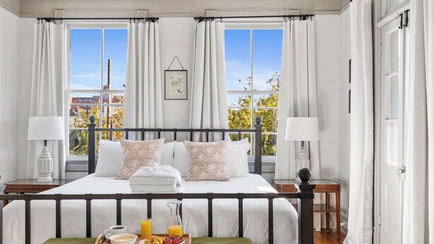 A neatly arranged bedroom with a bed, bedside tables, a tray with breakfast, and large windows with curtains. - Incredible 4bd House, 1 block to King w. Parking! (Charleston)