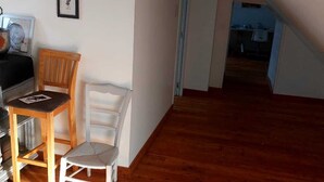 Une pièce avec un plancher en bois, une chaise blanche, une table en bois et un tableau encadré accroché au mur.