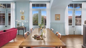 A dining room with a wooden table set for two, a red sofa, and a vase with flowers.